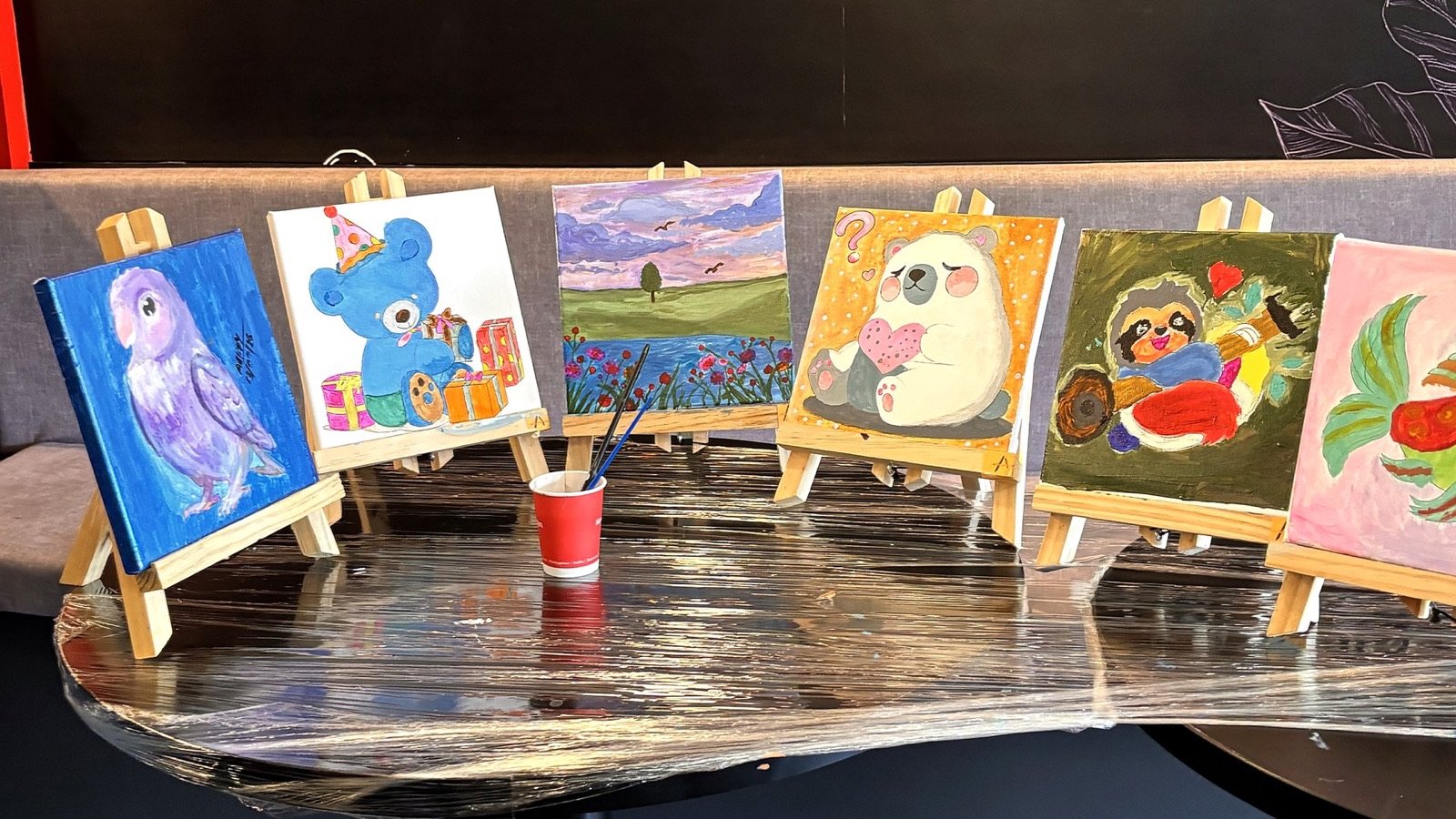 A row of finished paintings on wooden easels from a Sunday Paint Club session.