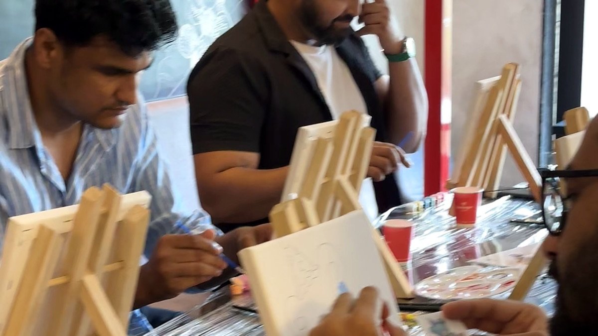 Guests painting side by side at a Sunday Paint Club session — easels and canvases on a covered café table, in mid-flow.