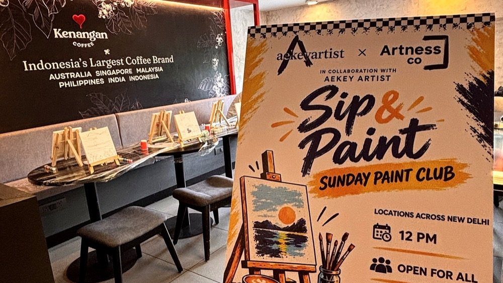 The Sunday Paint Club standee at Kenangan Coffee — easels lined up with sketched canvases in the background.